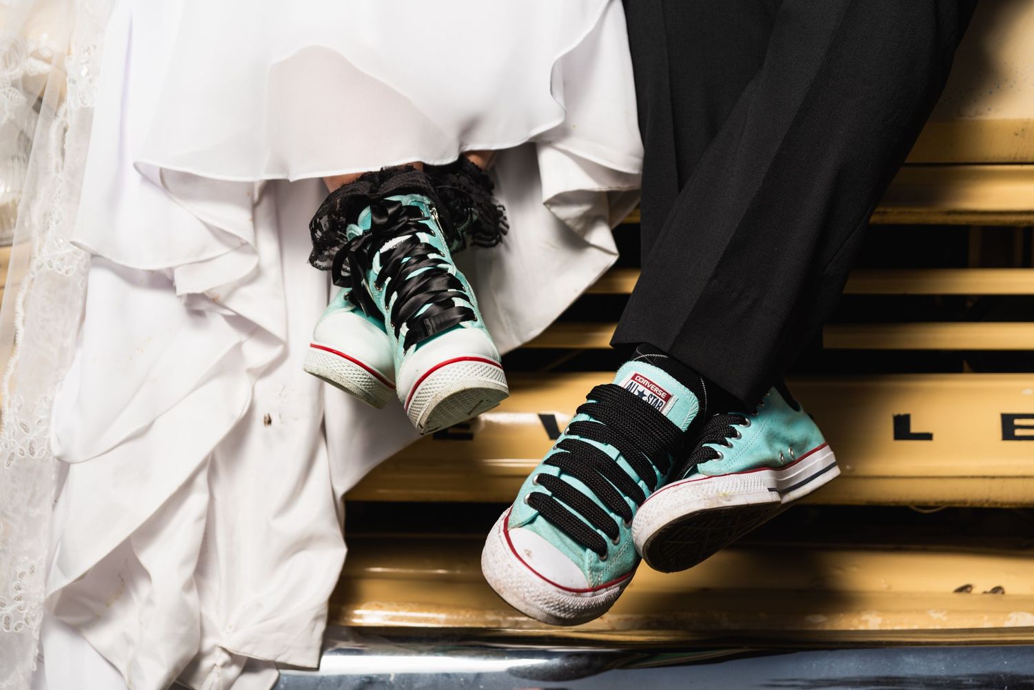 A close-up shot shows turquoise sneakers peeking out from under a white wedding dress on wooden stairs.