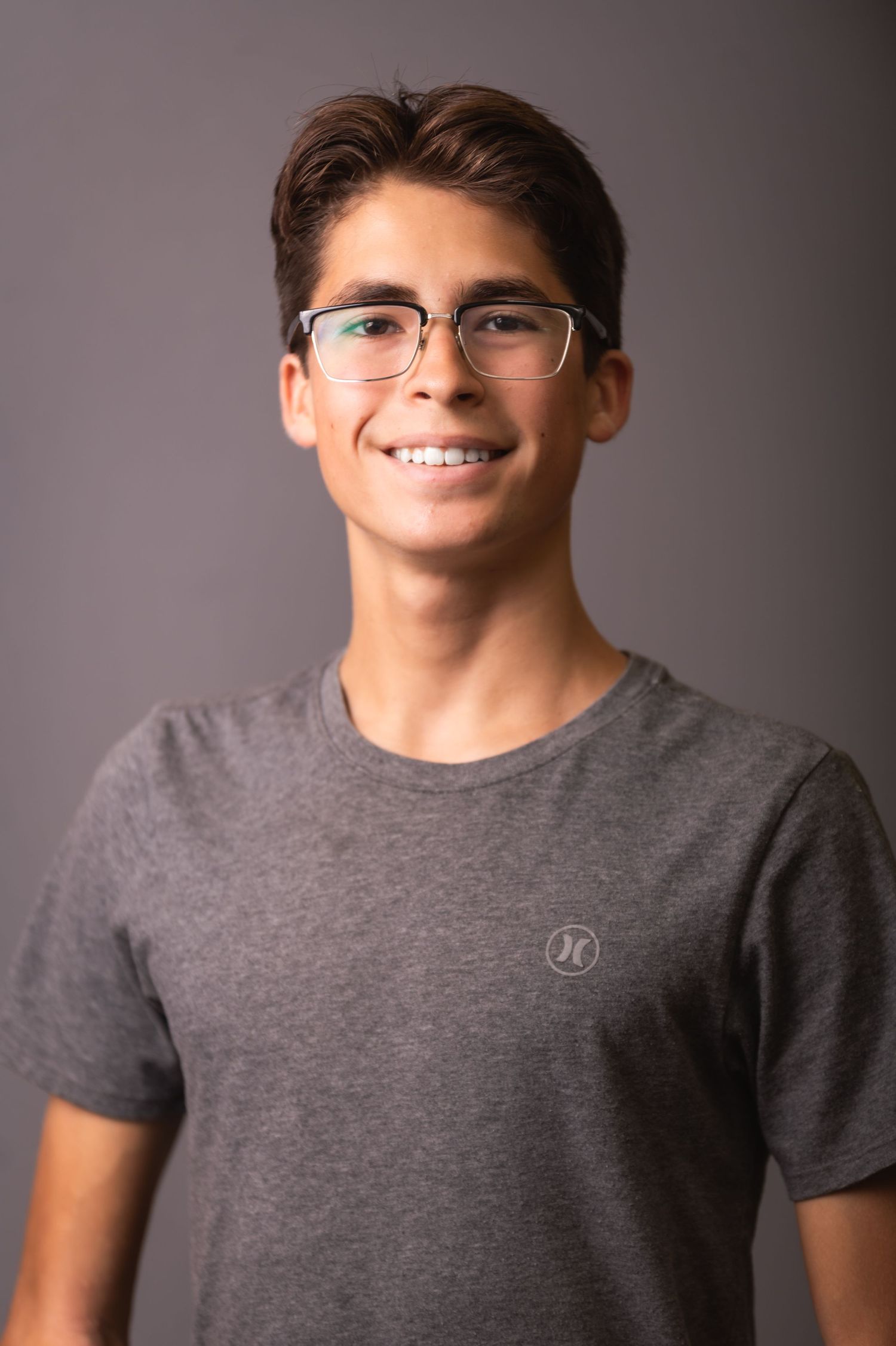 Studio portrait of young person in grey t-shirt and glasses against neutral background.