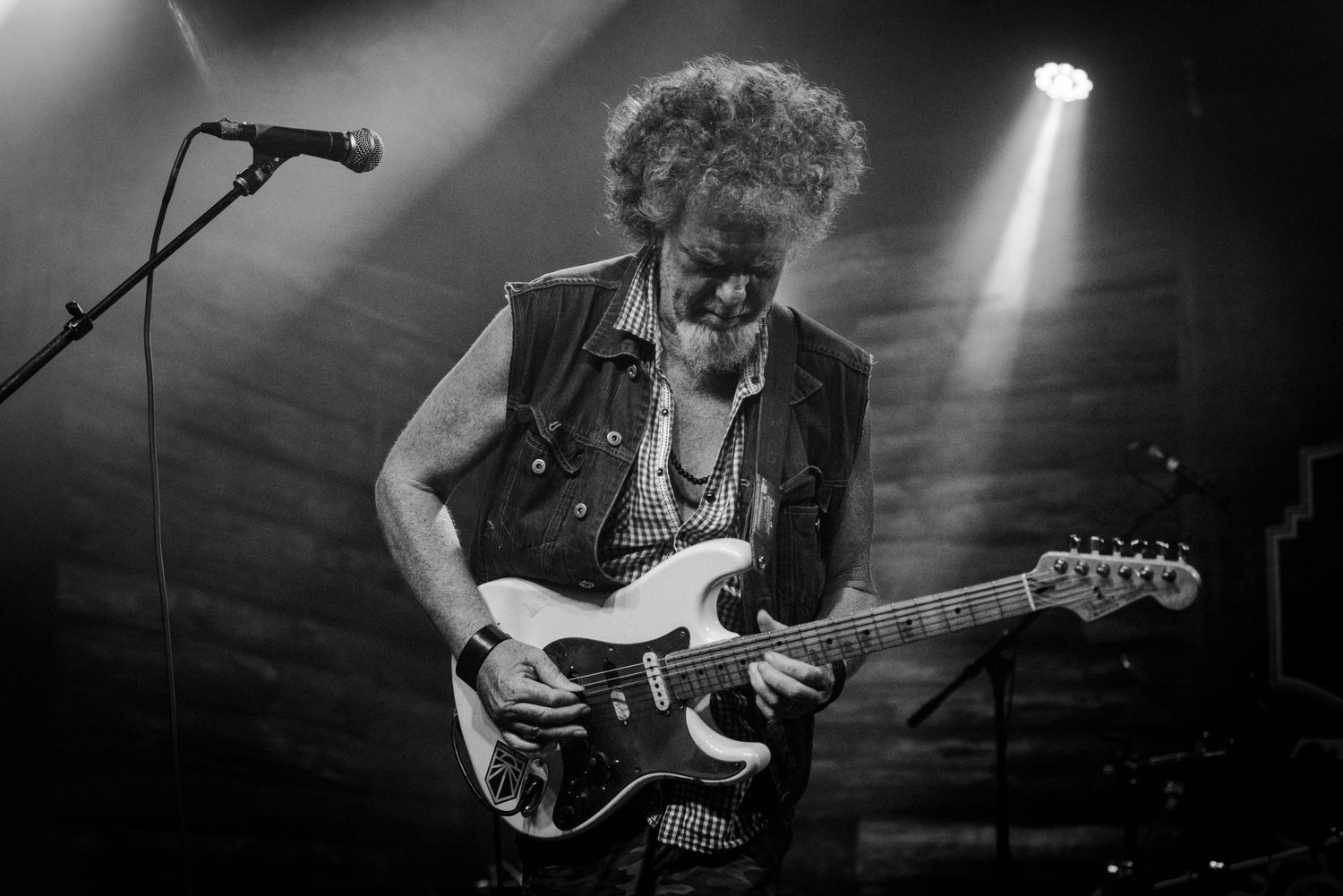 Black and white photo of guitarist performing with spotlight illumination on dark stage.