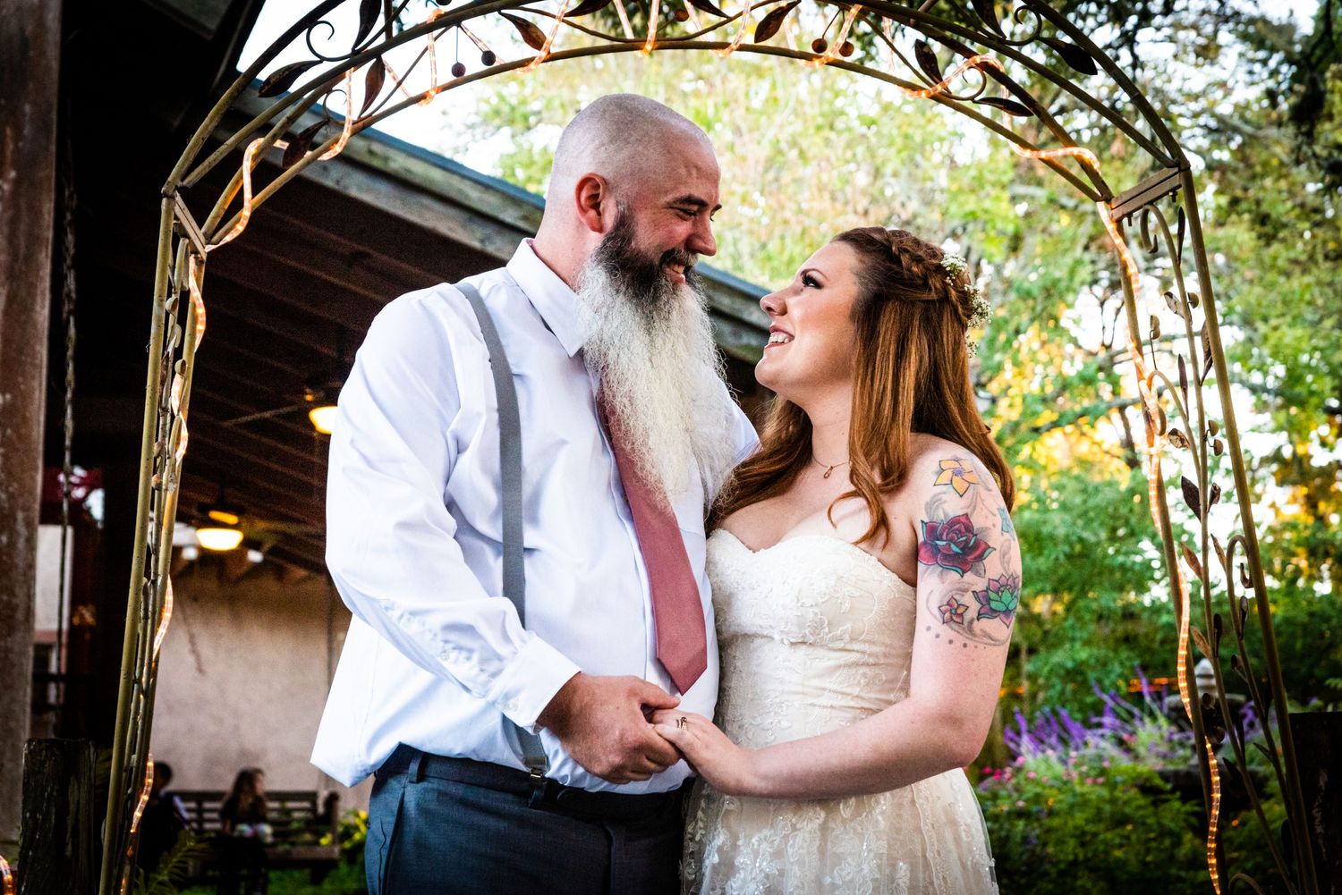 A couple shares an intimate moment under a decorative garden arch at their wedding celebration.
