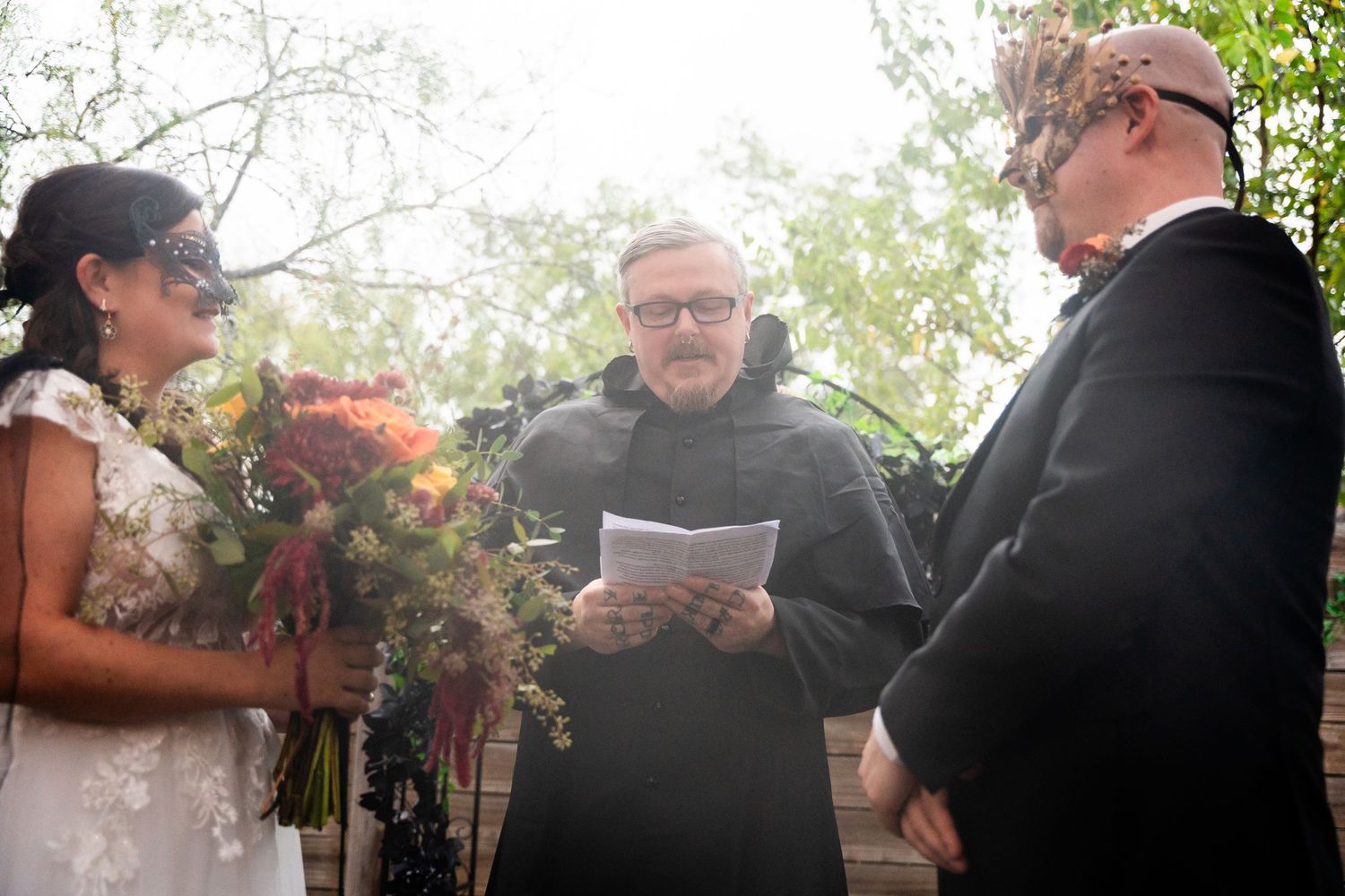 Wedding ceremony in progress under autumn trees with colorful bridal bouquet.