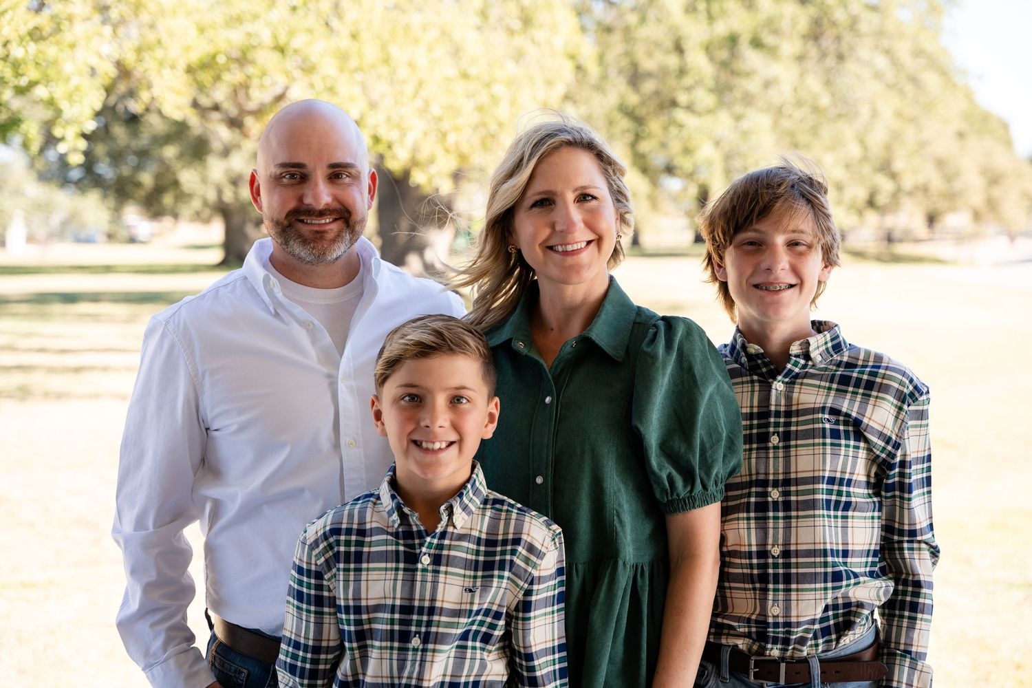 Family portrait taken outdoors with autumn trees in background.