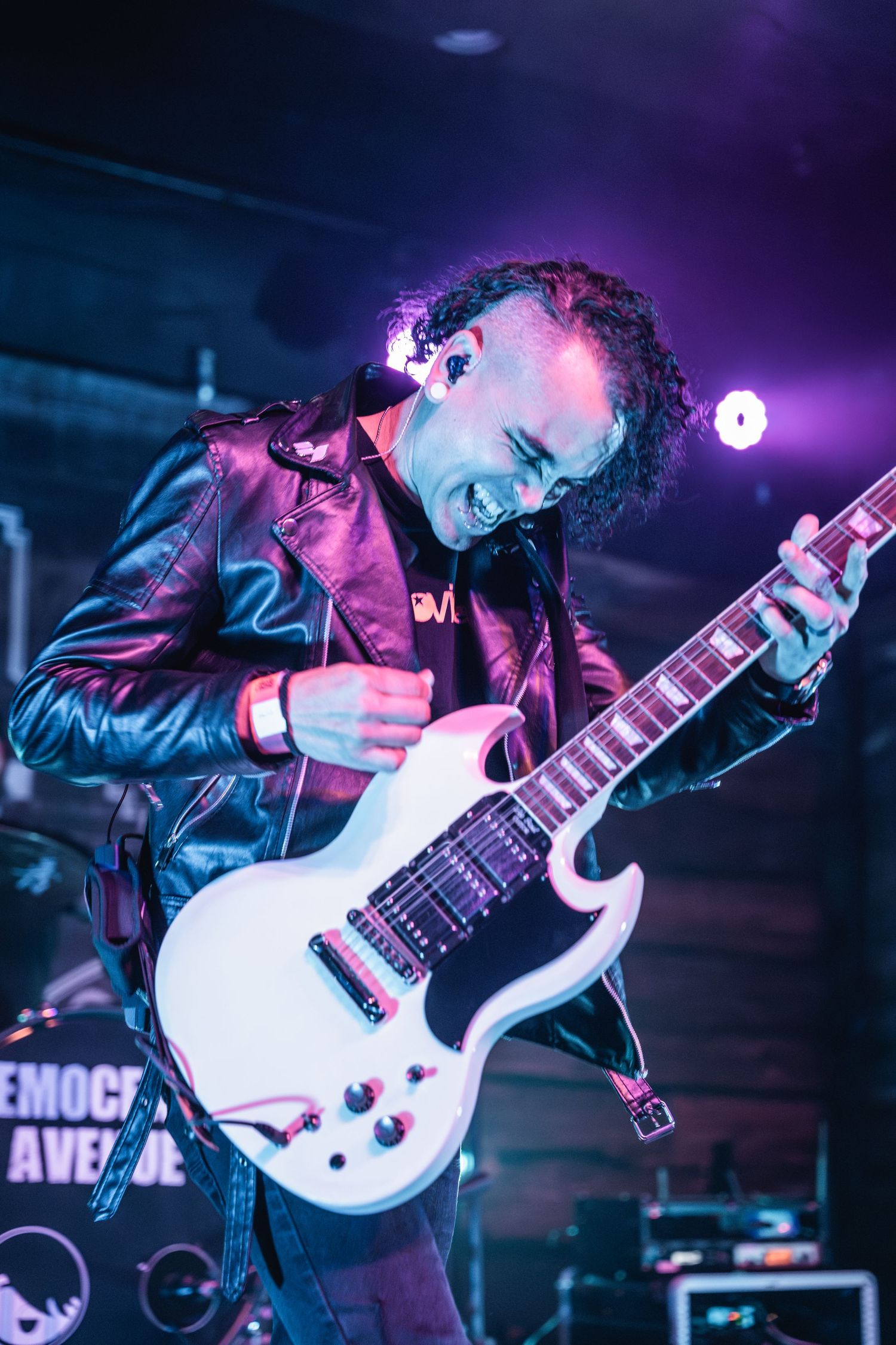 Musician playing white electric guitar with intense expression under stage lights.