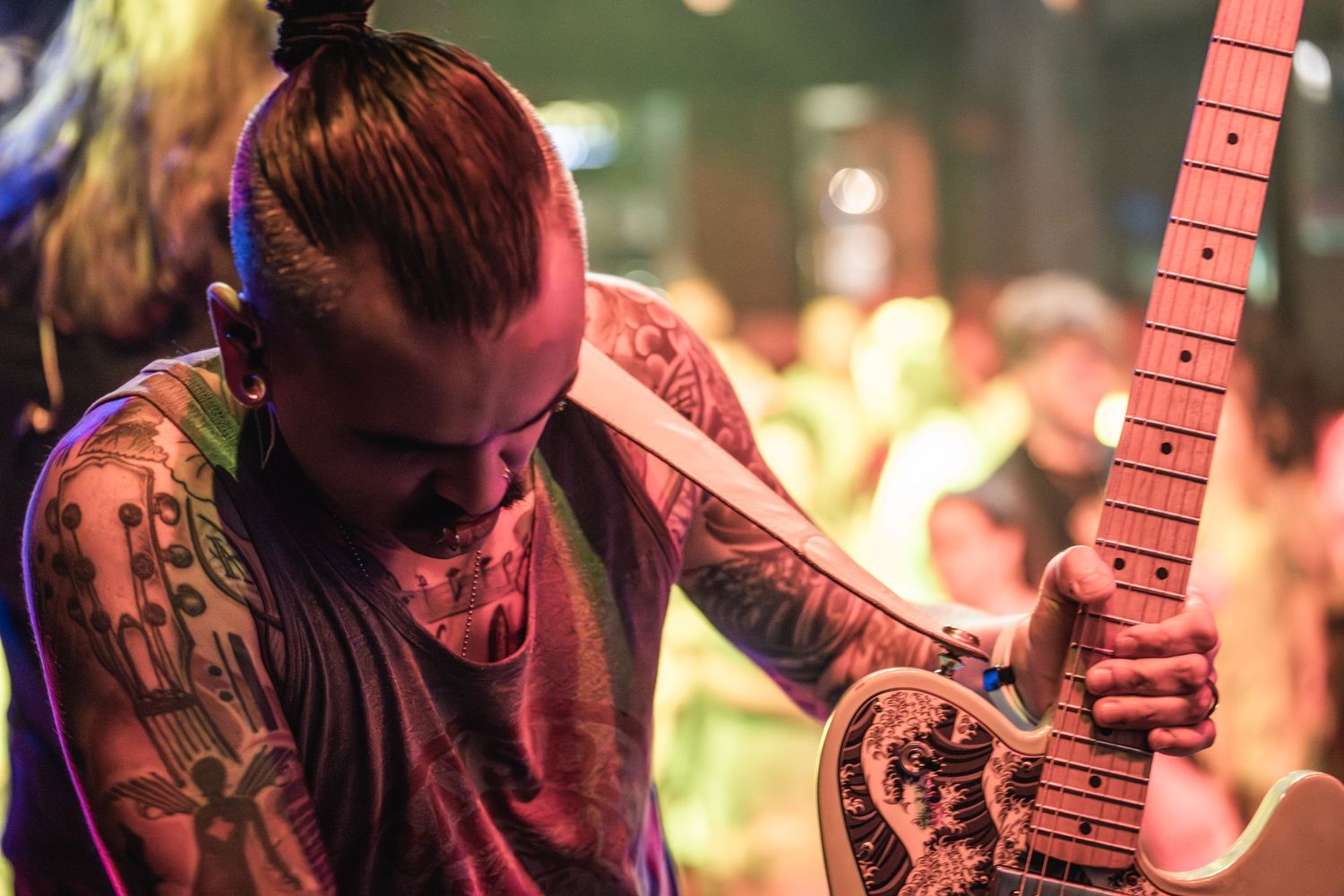 A tattooed musician plays guitar with intensity under stage lighting during a live performance.