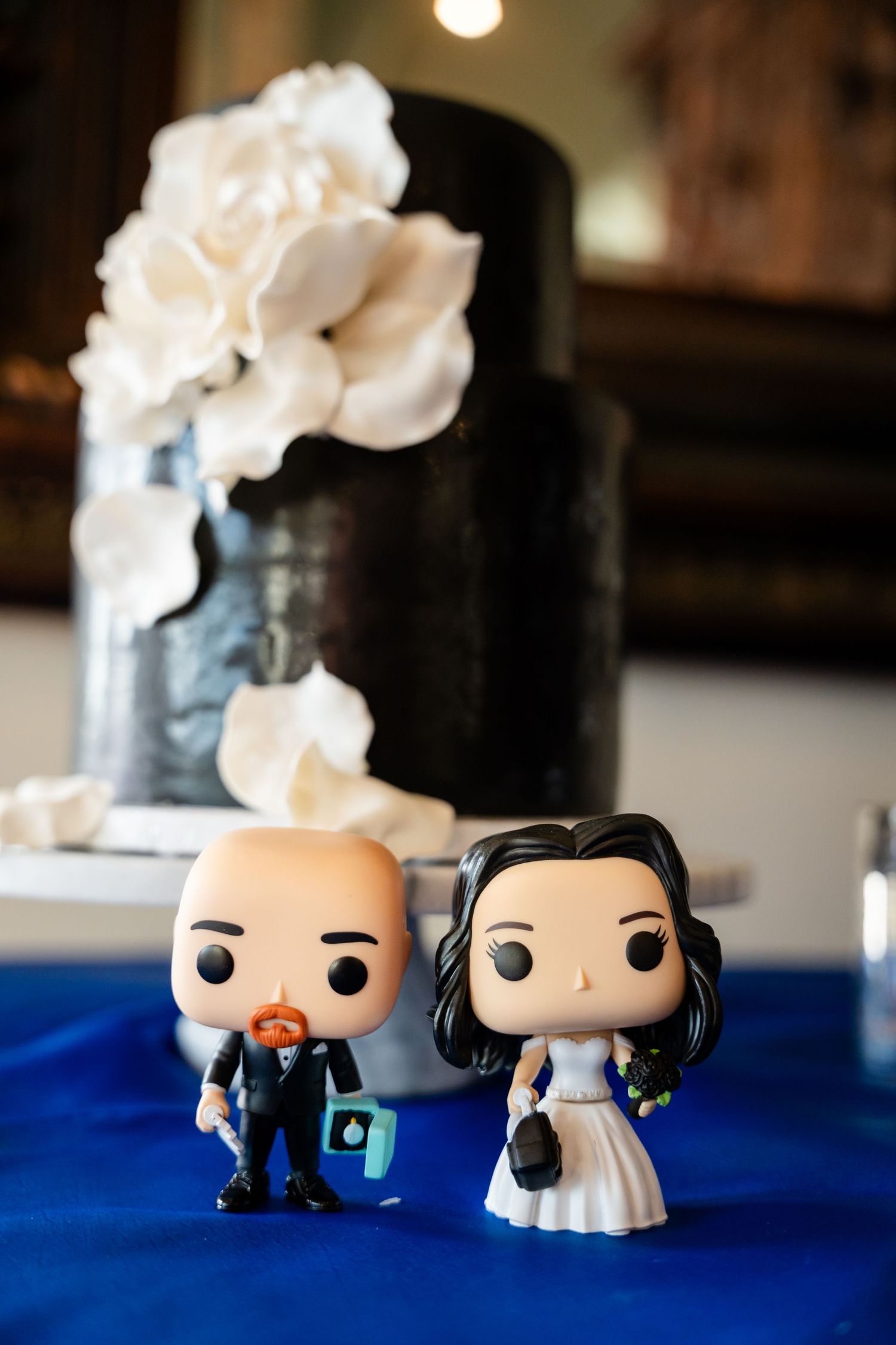 Wedding cake decorations with Funko Pop bride and groom figurines on blue tablecloth.