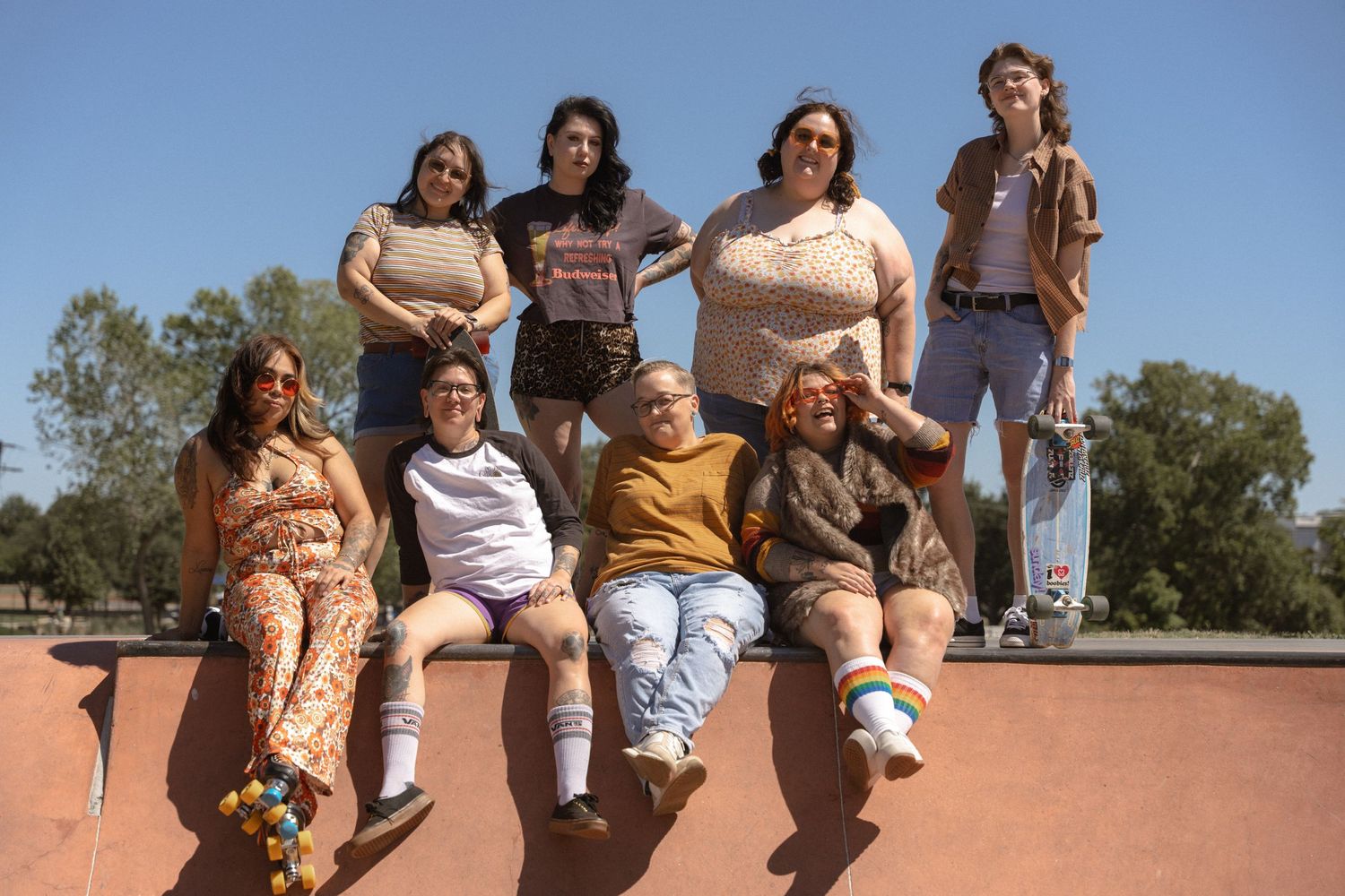 Group sitting on edge of skate ramp posing together on sunny day.