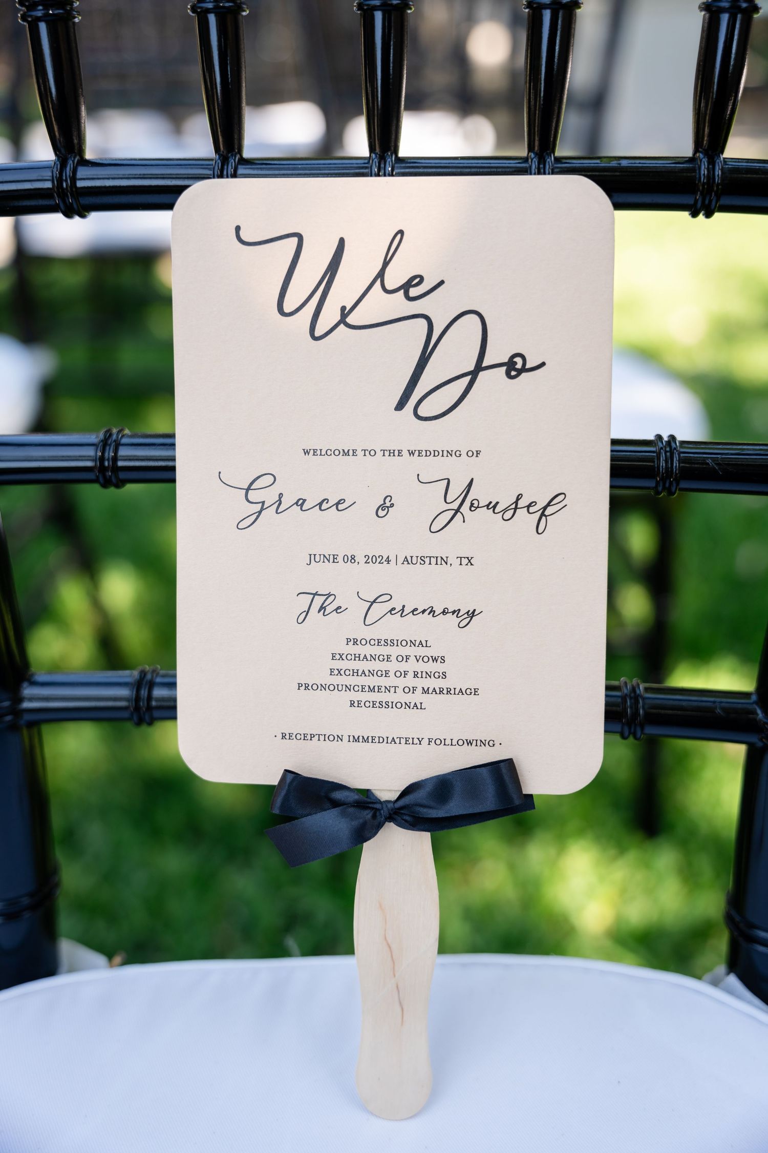 Wedding program fan with 'We Do' text and navy blue bow displayed on a chair.