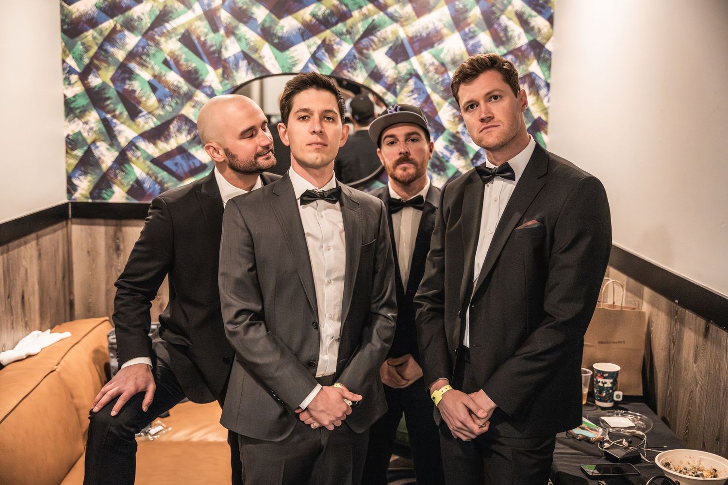 Four musicians in formal attire pose together backstage.