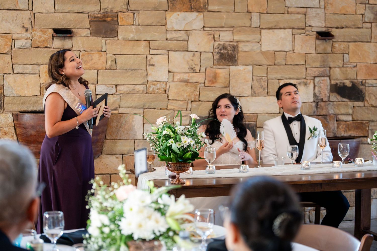 Wedding guests react emotionally while watching speeches during a wedding reception at a rustic stone venue.