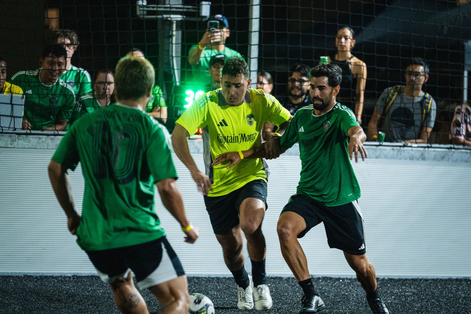 Players in yellow and green uniforms compete for ball control during night match.