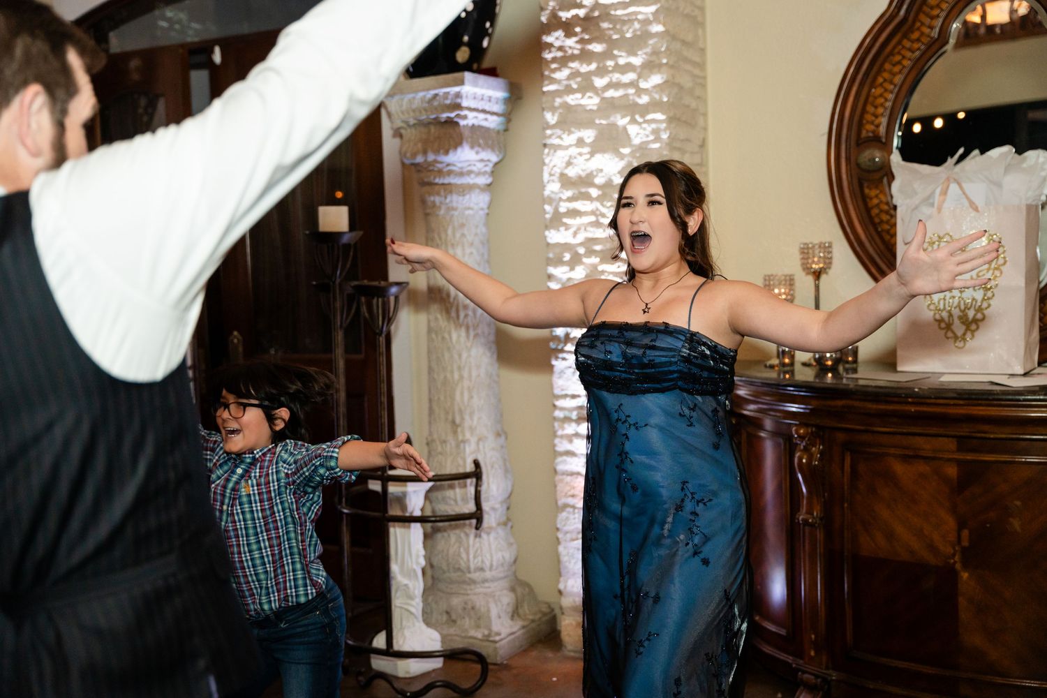 Dancers spread their arms wide during an upbeat moment at an indoor reception.