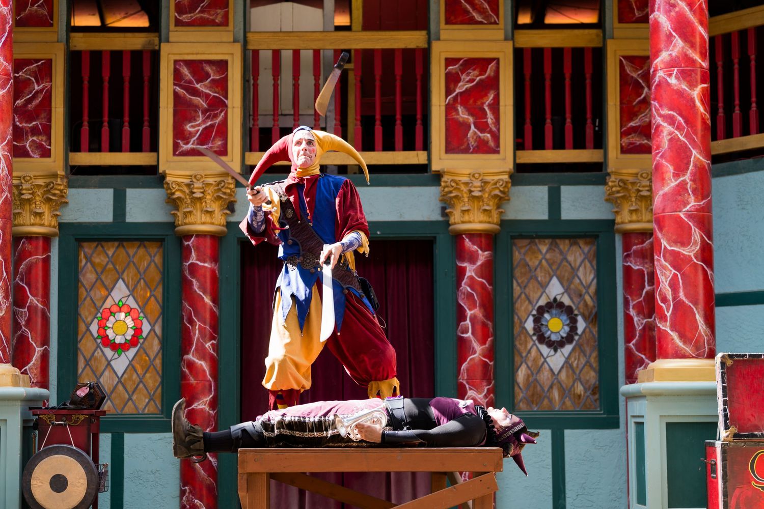 A performer in colorful Renaissance attire balances on a raised platform during a festival show.