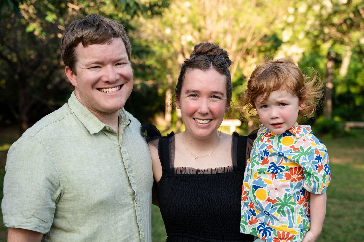 Small family group poses together outdoors in casual summer attire.