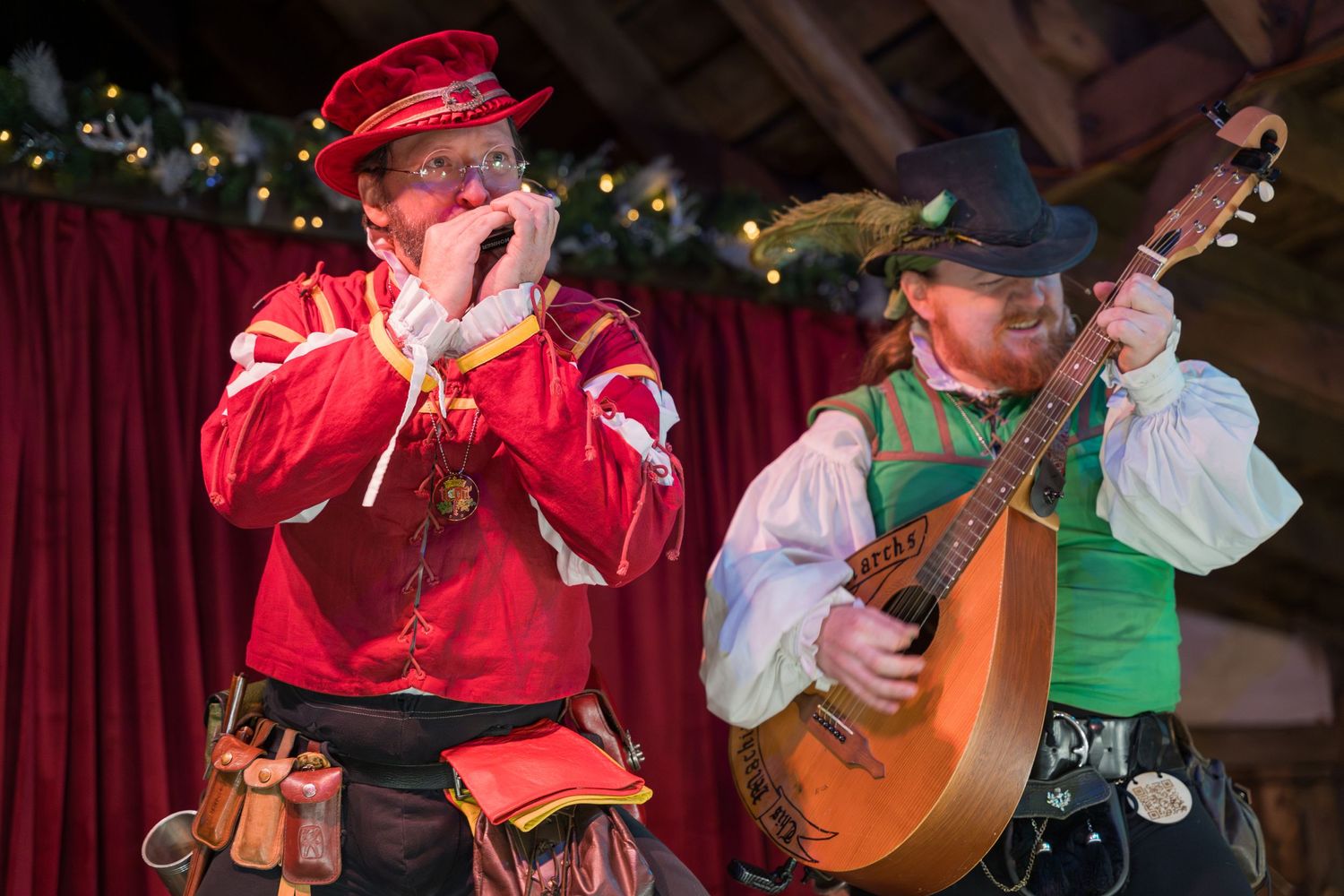 Musicians in Renaissance attire performing with traditional instruments against red curtain.