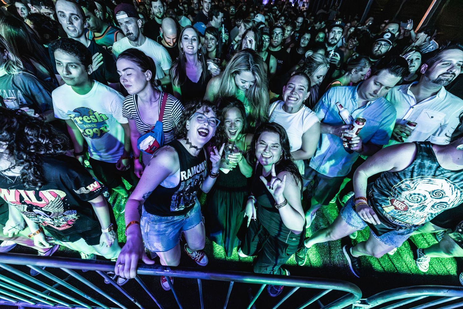 Energetic crowd packs the front row at concert venue under colorful lighting effects.