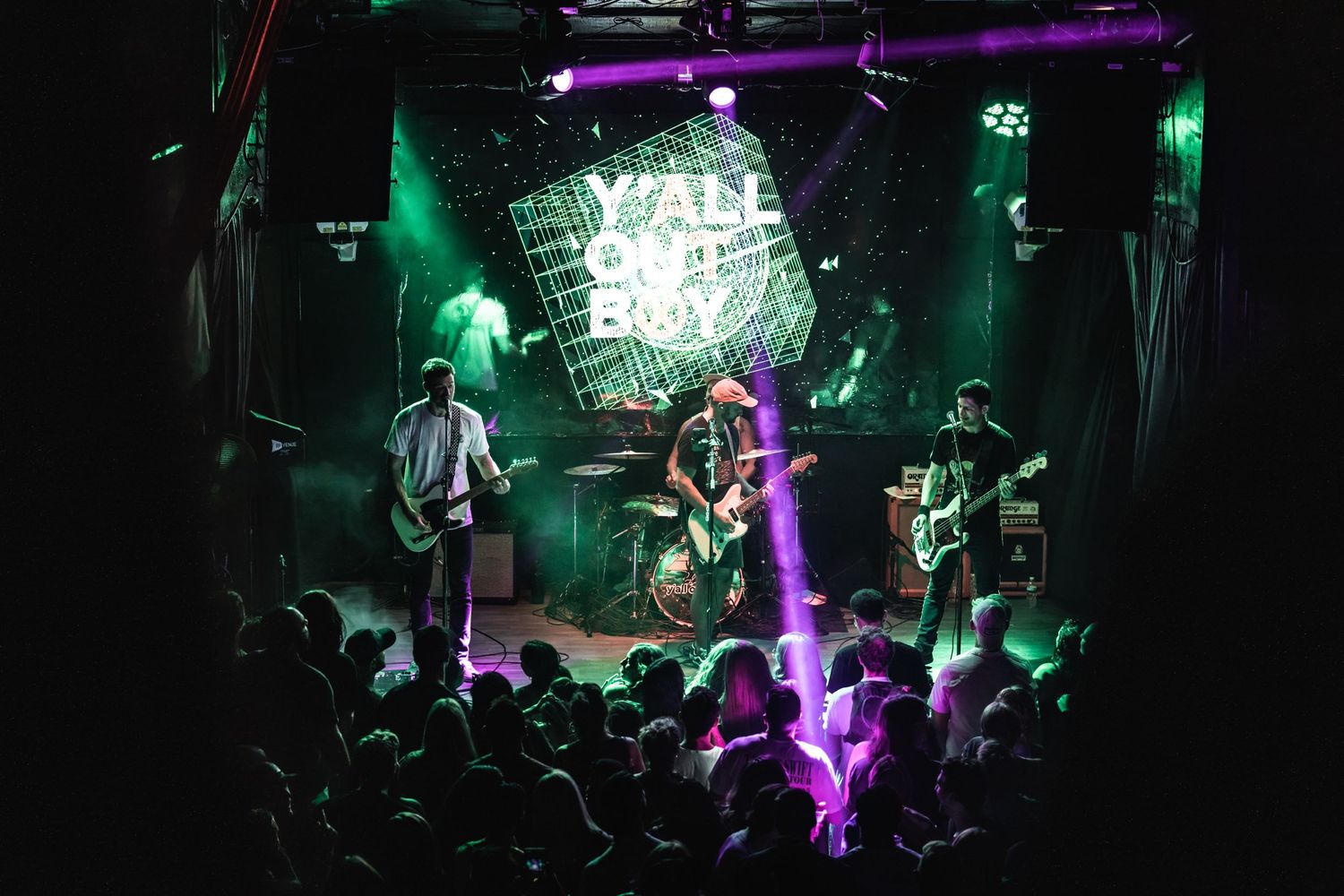 Rock band performing live on stage with green lighting and excited crowd.