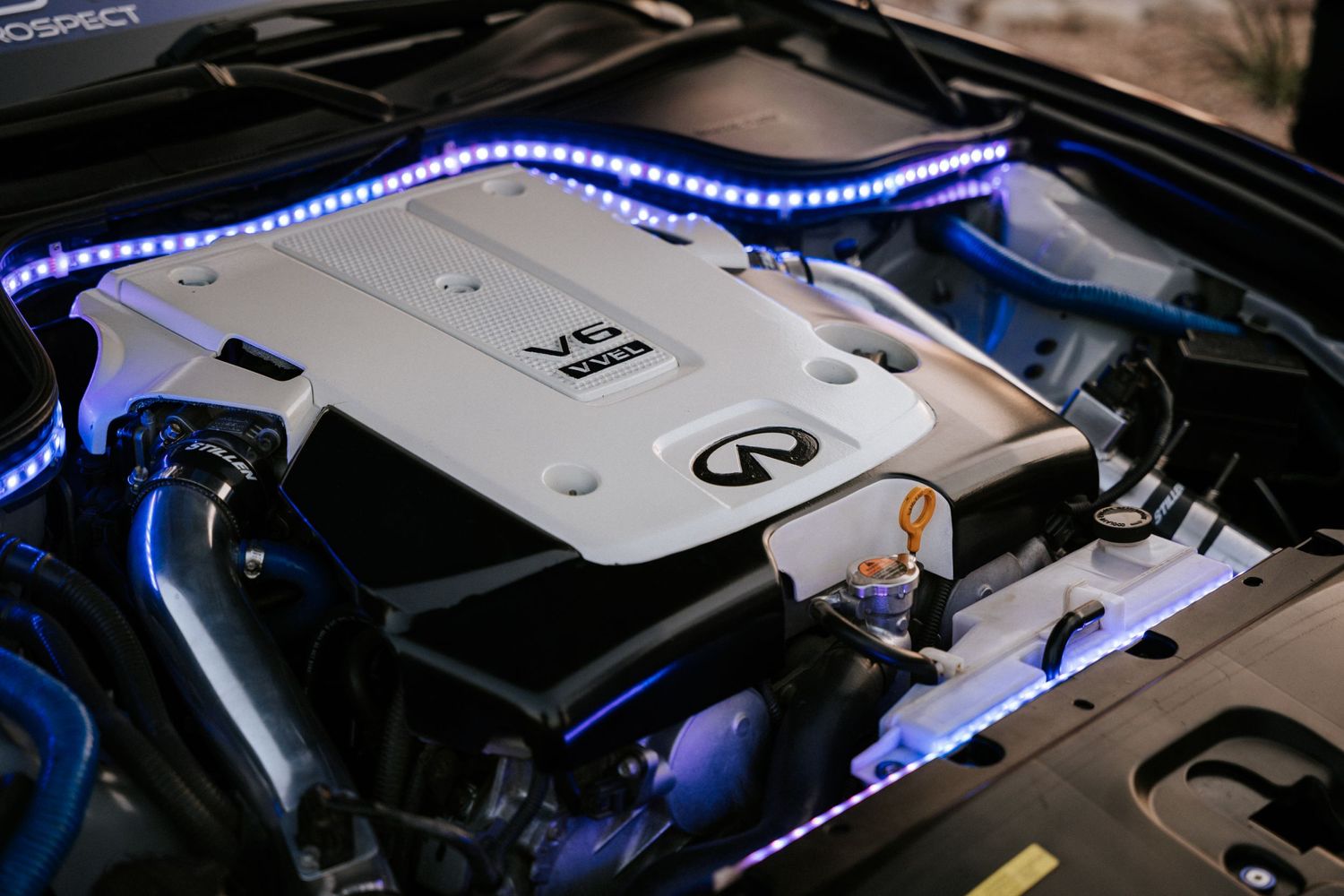Infiniti engine bay illuminated with blue LED strip lighting showing performance modifications.