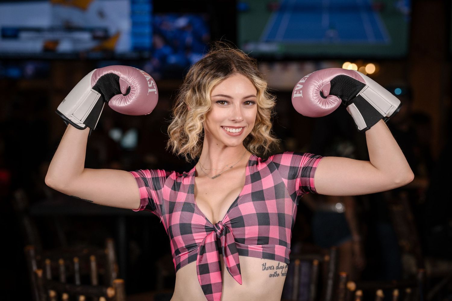 Model shows strength pose with pink boxing gloves and plaid crop top.