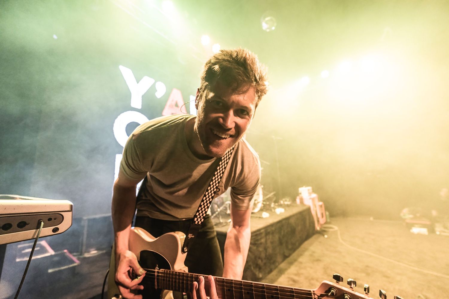 Musician playing guitar on stage with yellow and green mood lighting effects.