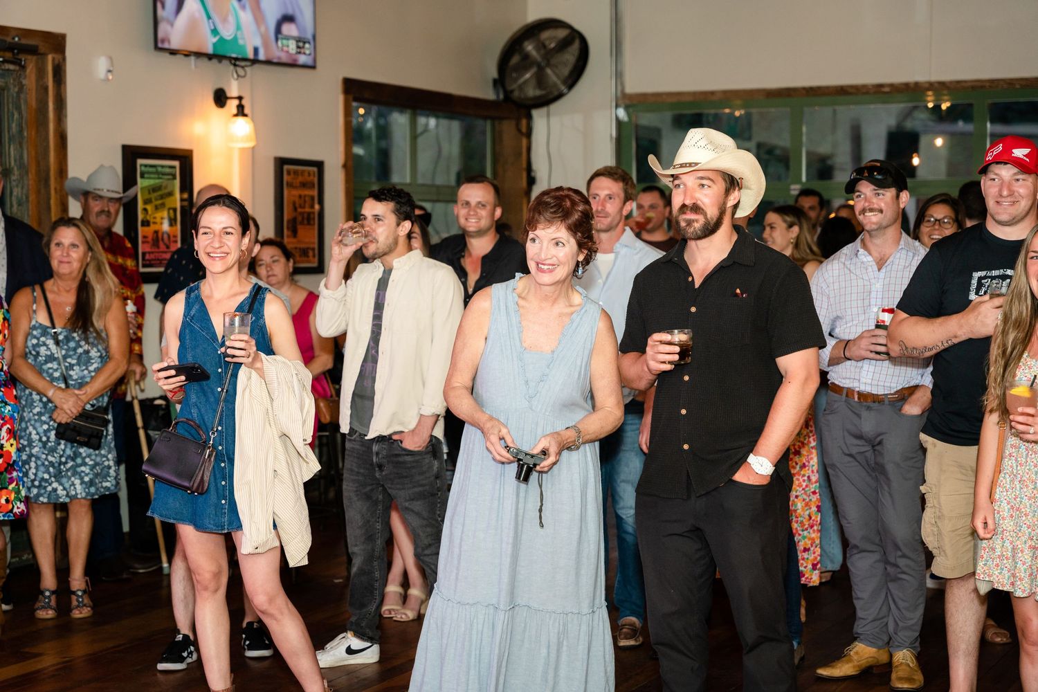 Large group of guests mingling at an indoor social gathering with drinks.