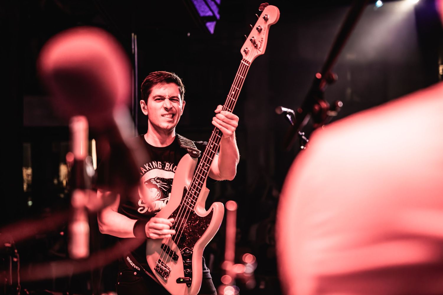 Bass player performing on dimly lit stage with microphone in foreground.