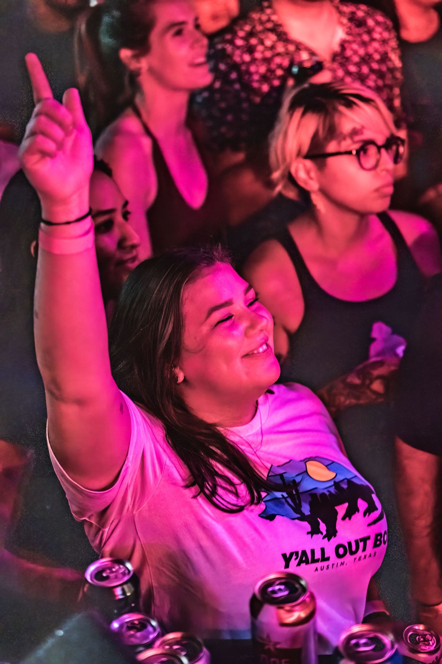 Concert attendee in pink shirt enthusiastically dances and points upward in magenta lighting.