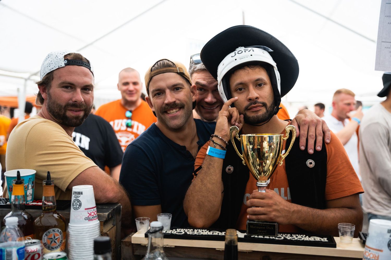 Group celebrating with a trophy at outdoor drinking festival under white tent.