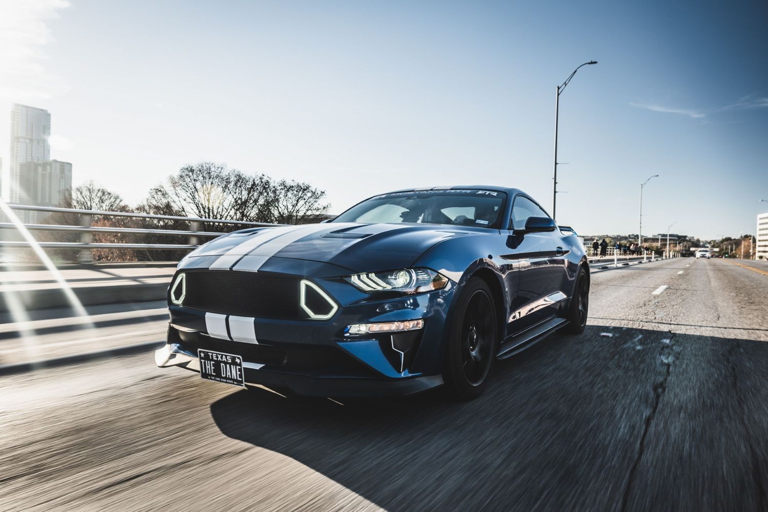 Blue Ford Mustang GT with racing stripes photographed in dynamic motion on highway.