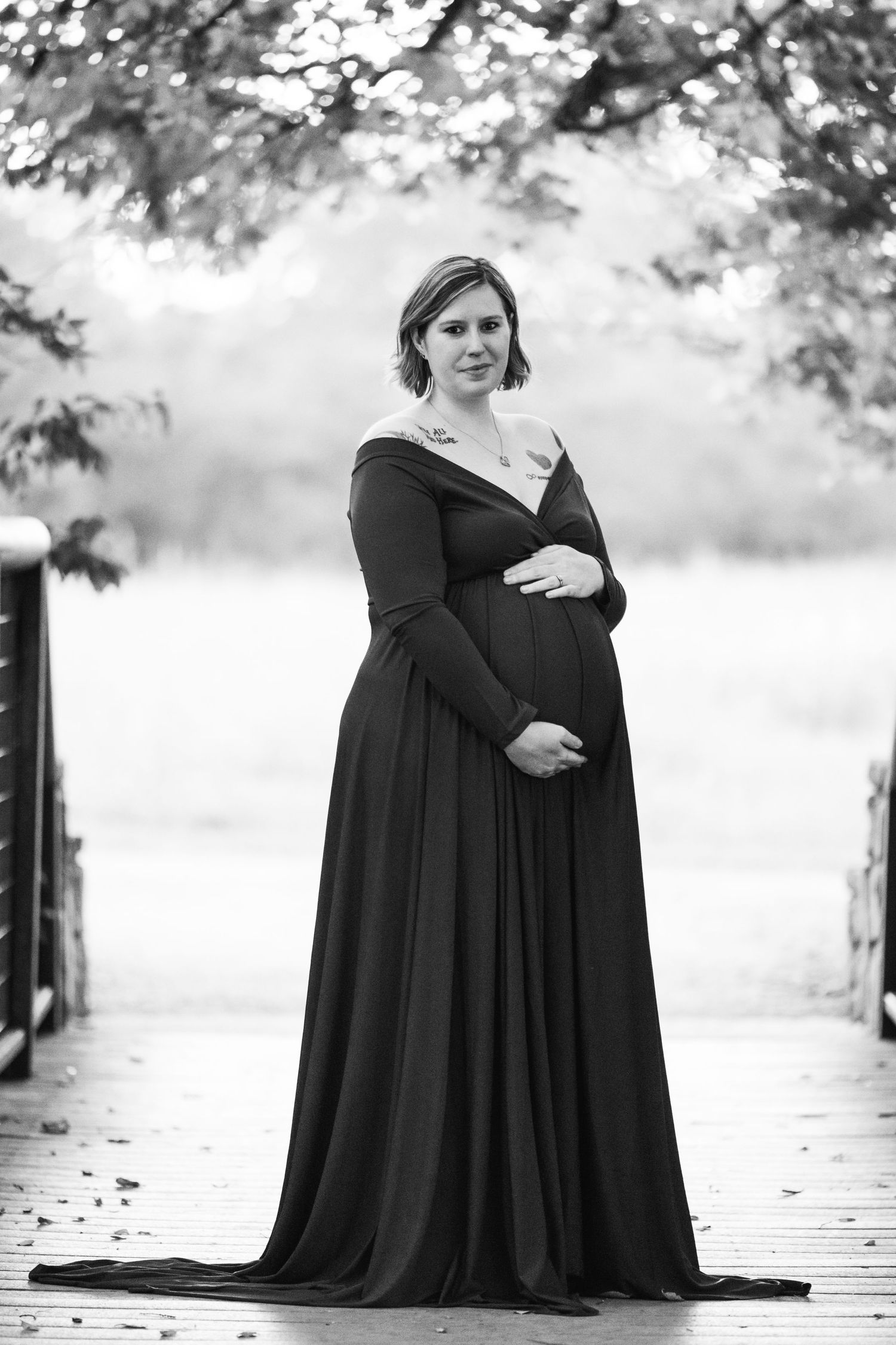 Black and white maternity portrait on wooden bridge with dramatic lighting.