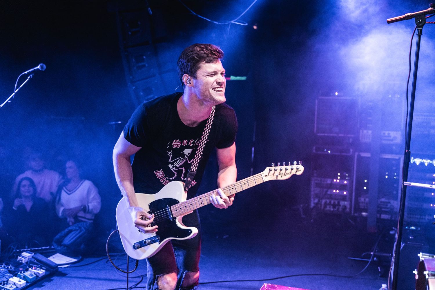 Guitar player performing energetically on stage with blue lighting effects at concert venue.