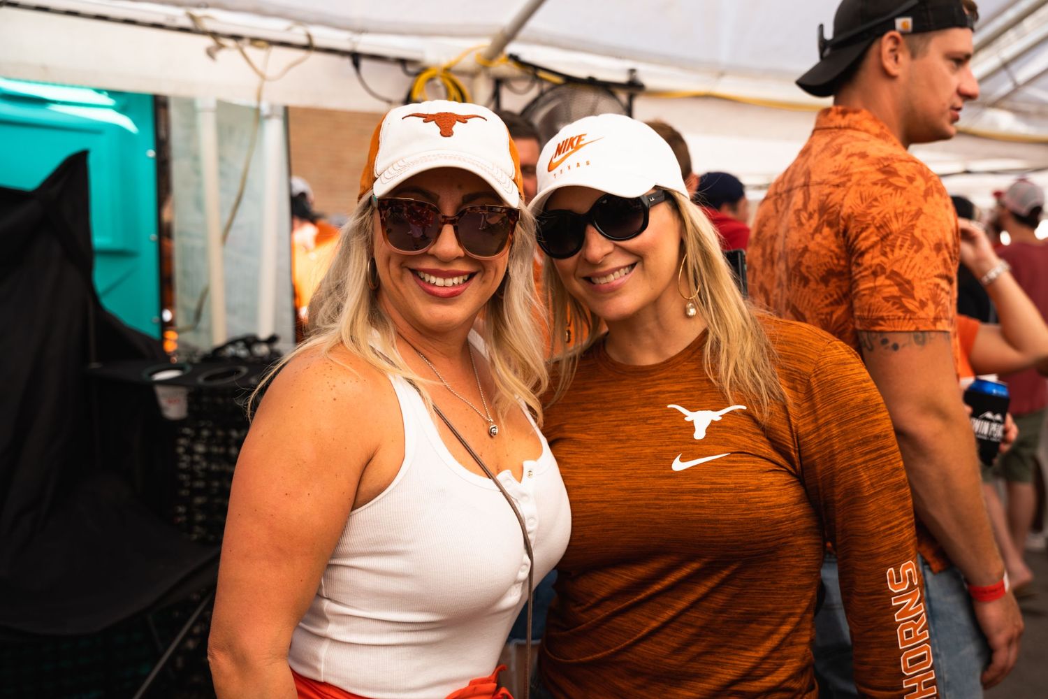 Two fans in Texas Longhorns gear smile together at an outdoor sporting event.