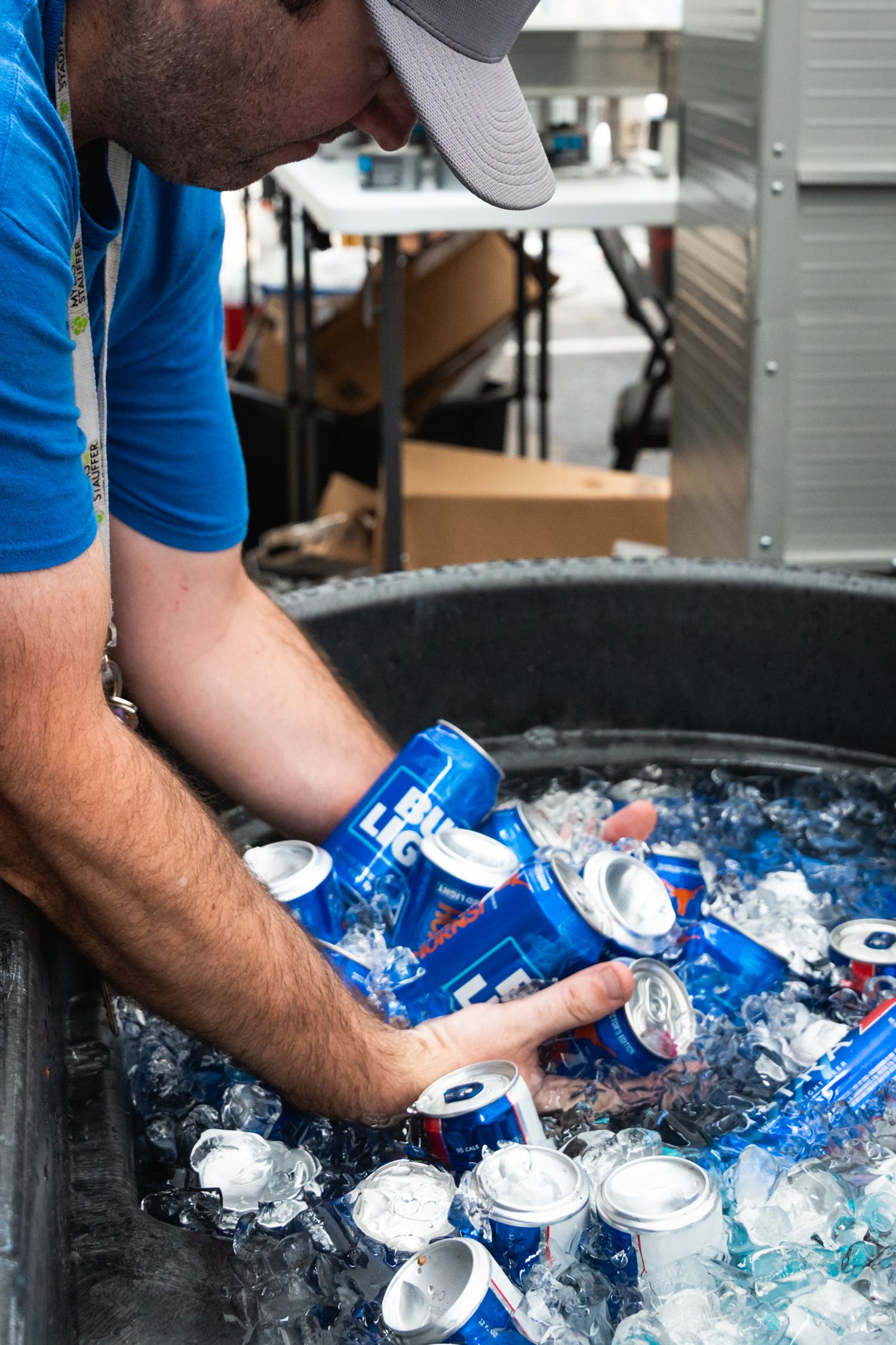Person in blue shirt reaching into ice cooler filled with Bud Light cans.