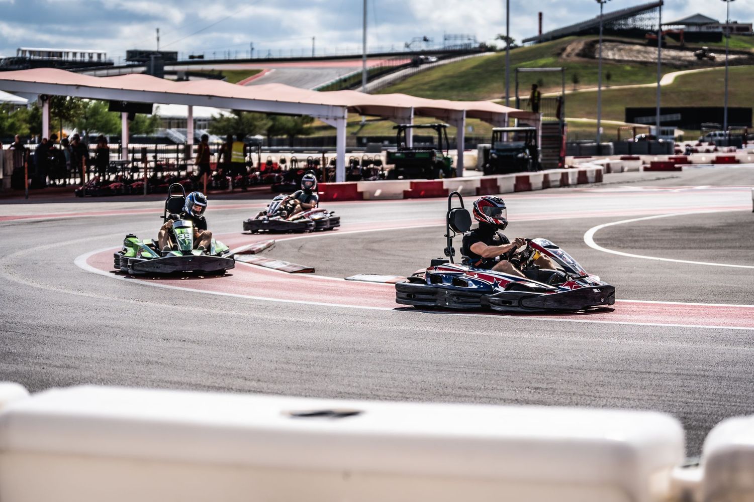 Multiple go-karts racing through a curve on an outdoor track under covered area.