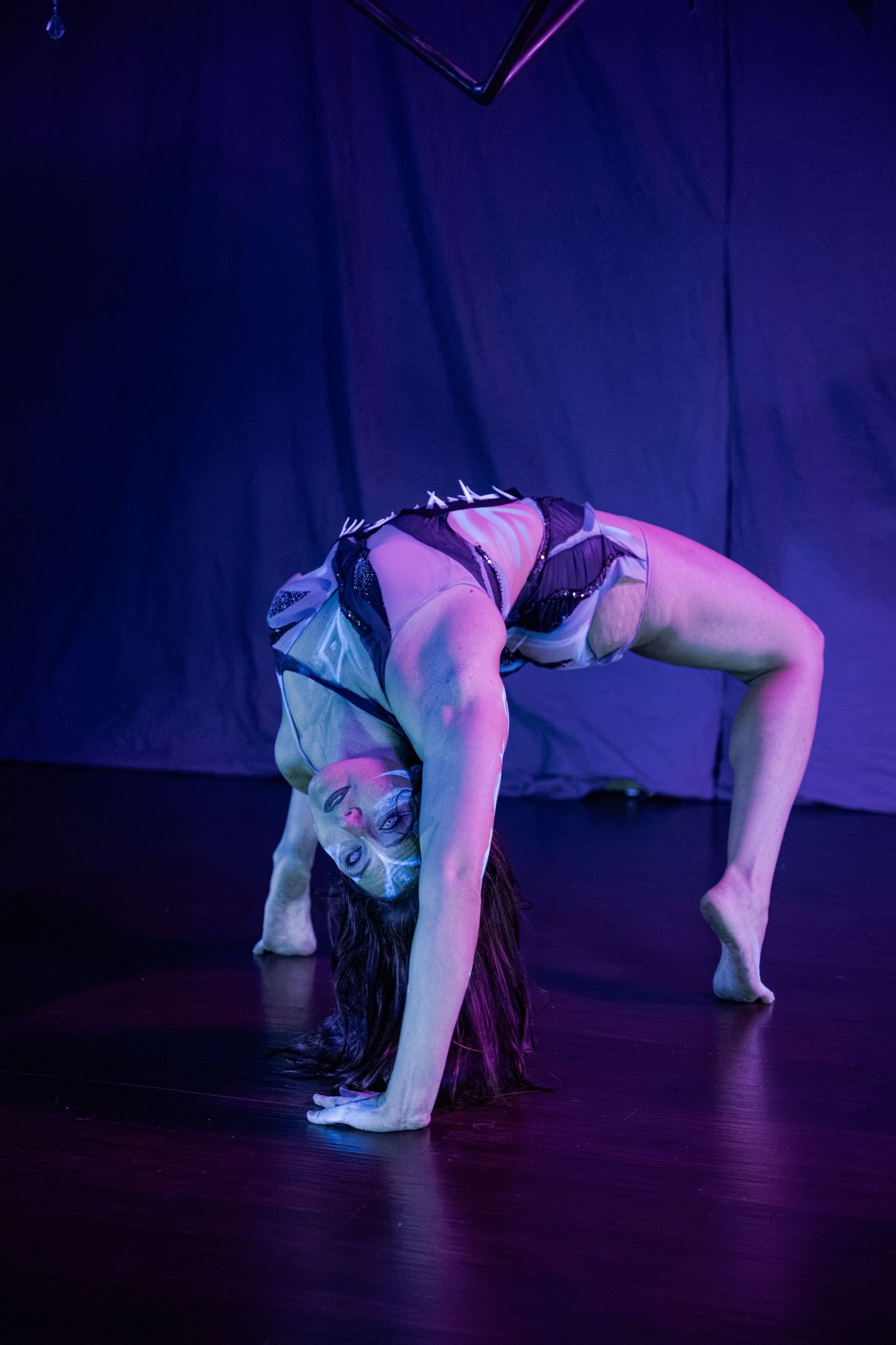 Flexible contortionist performs a backbend on stage under purple lighting during a live performance.