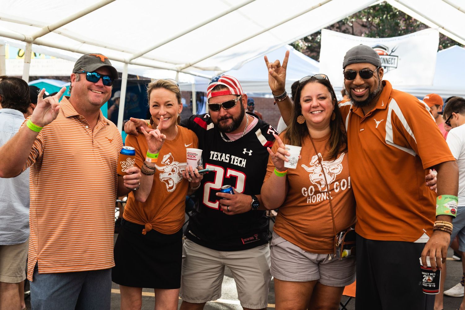 A group of University of Texas fans in burnt orange shirts celebrate and pose together at a tailgate party.