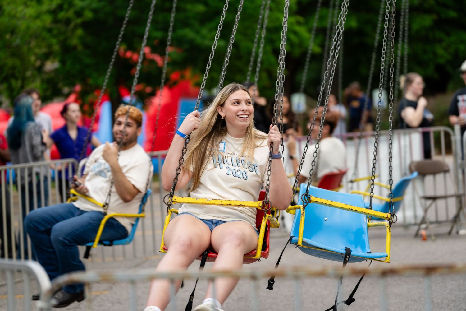 Young woman enjoying a chain swing carnival ride at an outdoor festival with crowds in the background.