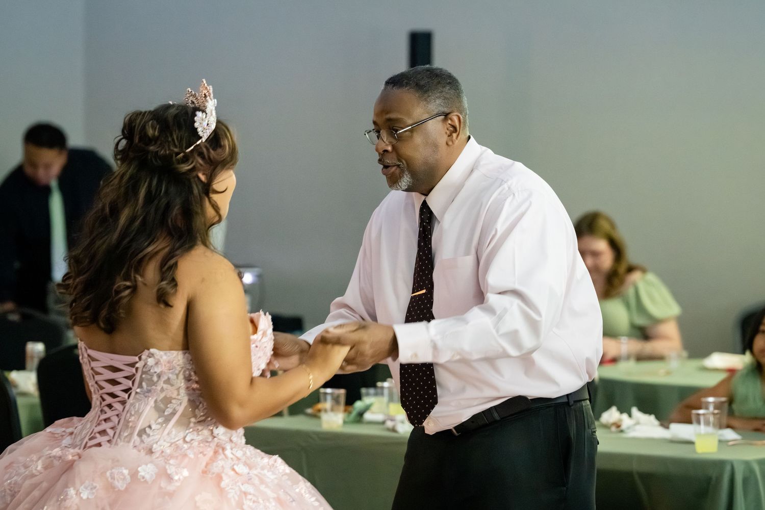 A man in a pink shirt dances with a girl in a pink quinceañera gown at a celebration event.