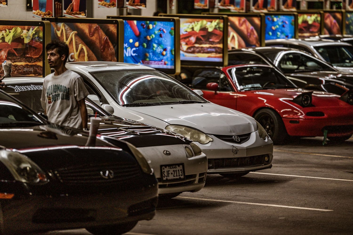 Modified sports cars including Mazda and red Miata parked at automotive meetup with decorative backdrop.