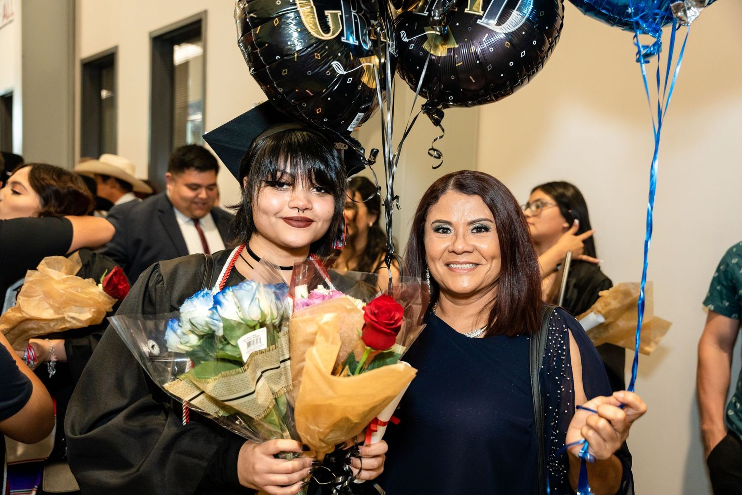 Graduate holding flowers and balloons celebrates with companion after ceremony.