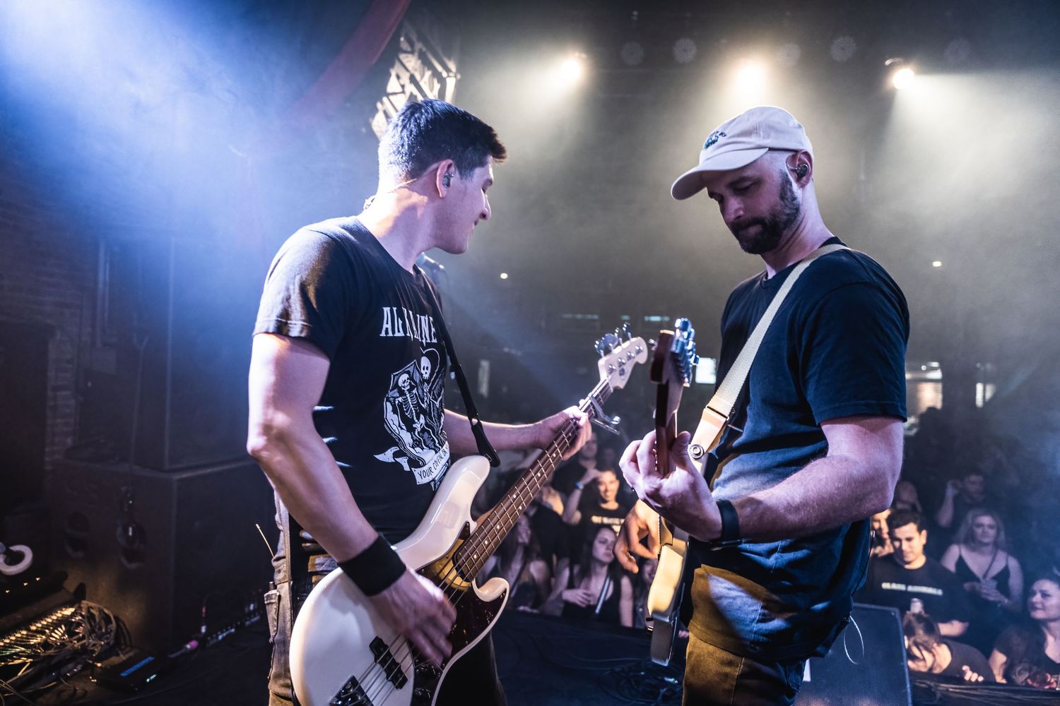 Two musicians playing guitars together during an energetic performance under blue stage lights.