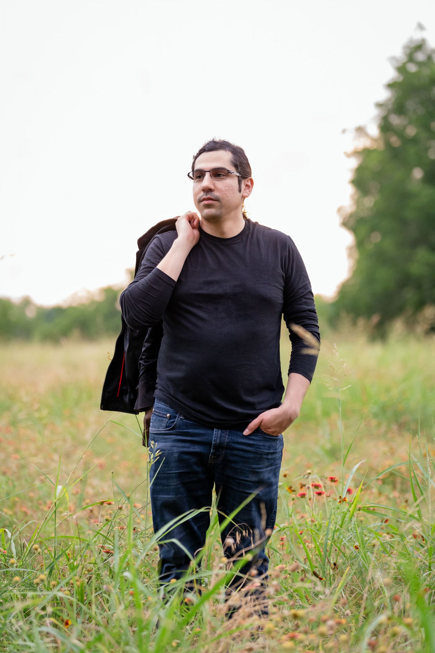A person stands in a grassy field at dusk wearing a black sweater and jeans.