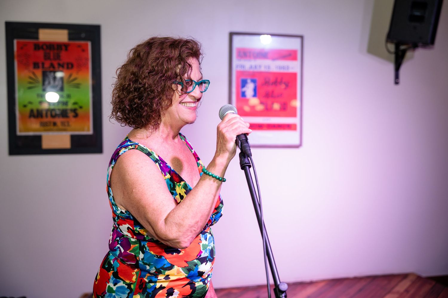 Woman in a colorful dress speaking into microphone at indoor venue with posters on wall.