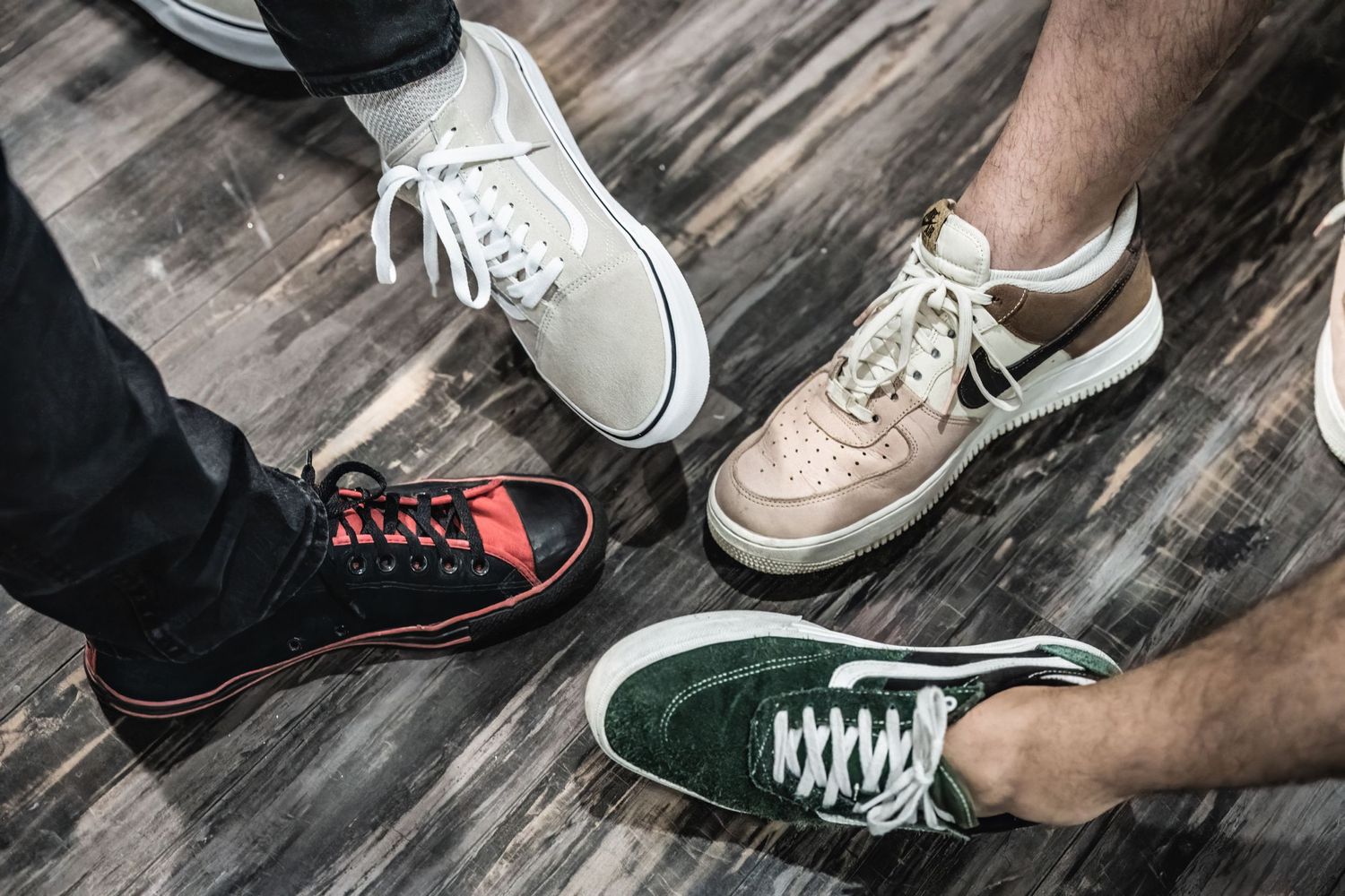 Various casual sneakers and shoes on wooden floor showing different styles and brands.