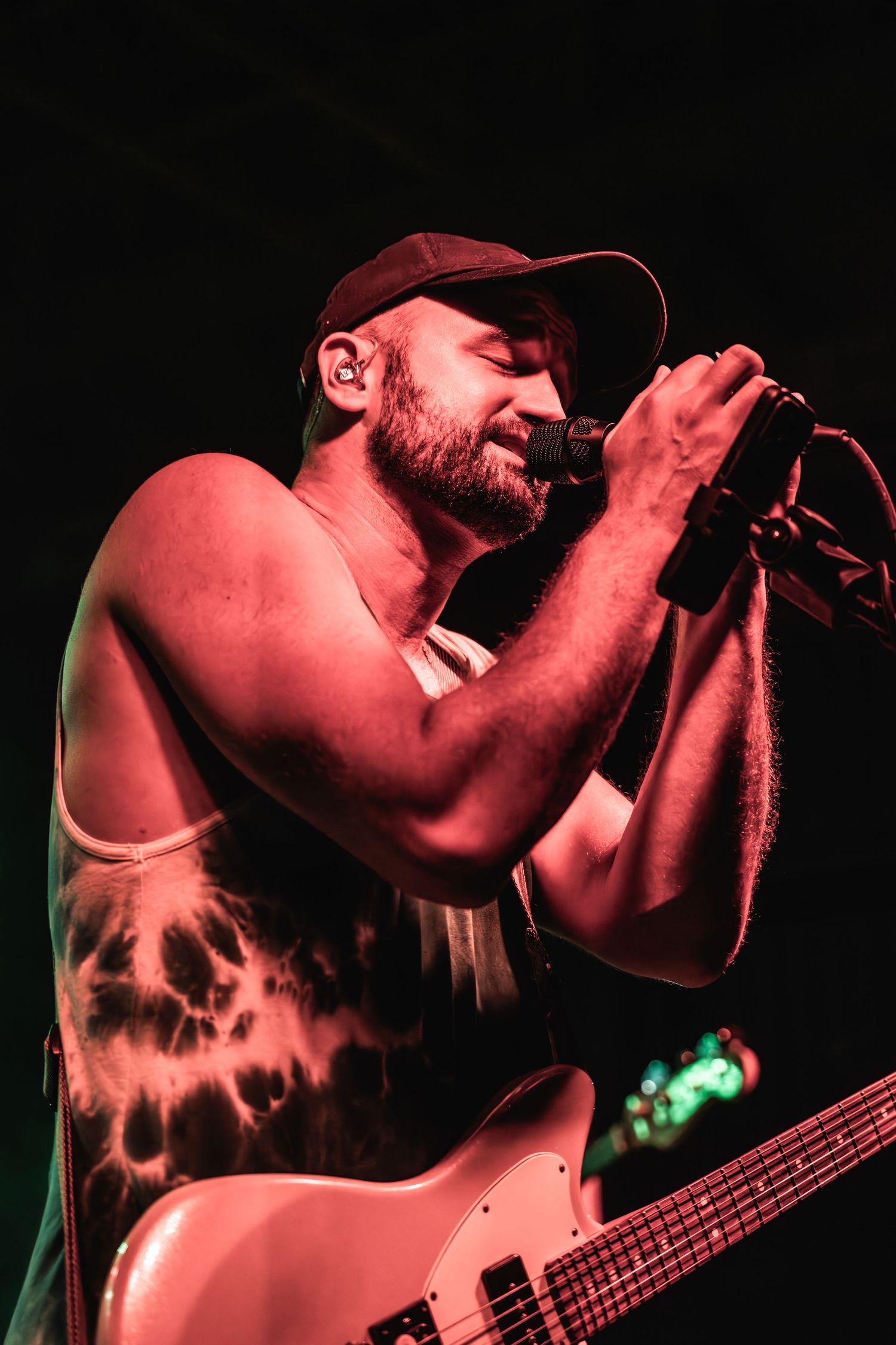 Concert performer singing passionately into microphone under warm red stage lighting.