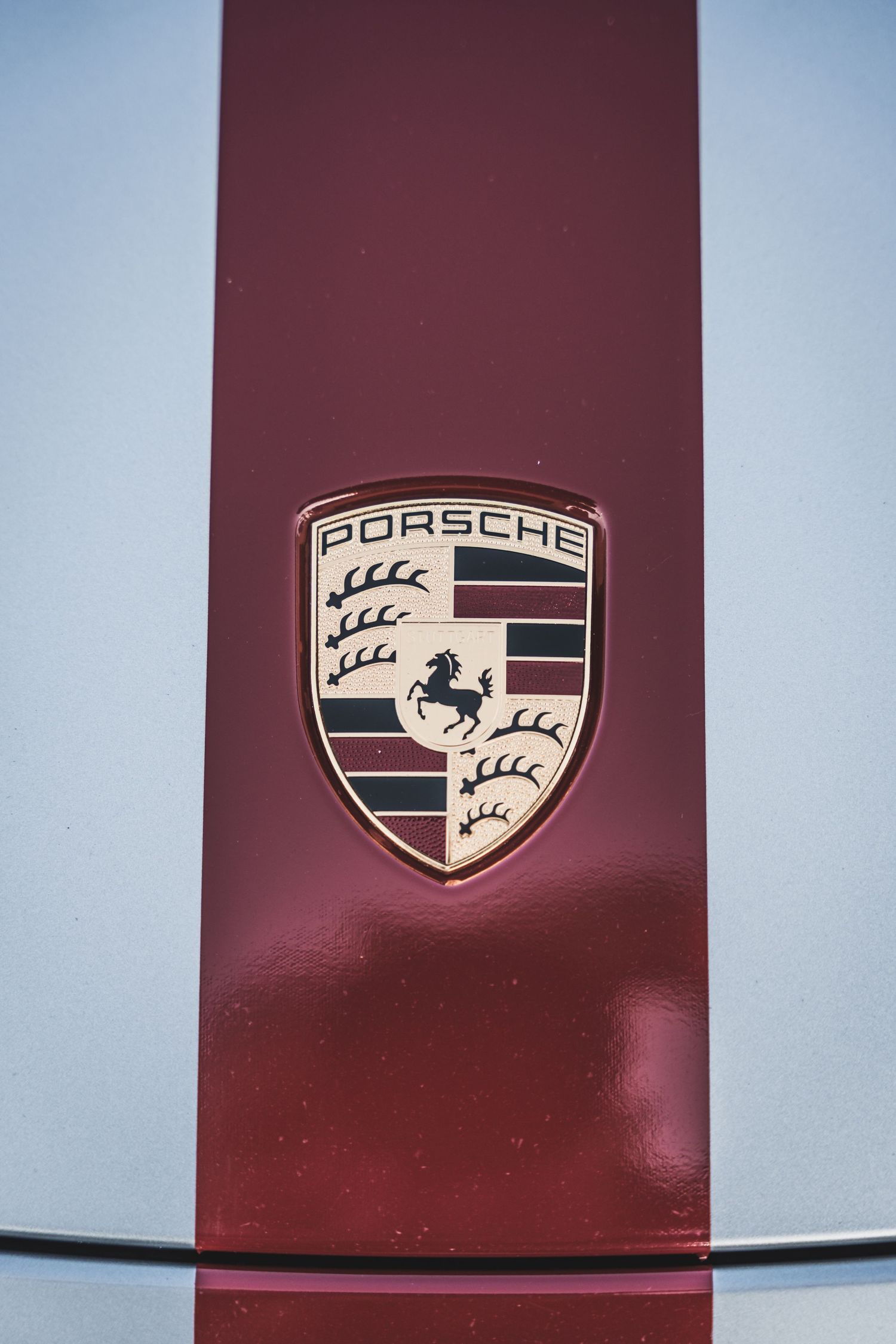 Detailed shot of the iconic Porsche emblem on a silver car with burgundy stripe.