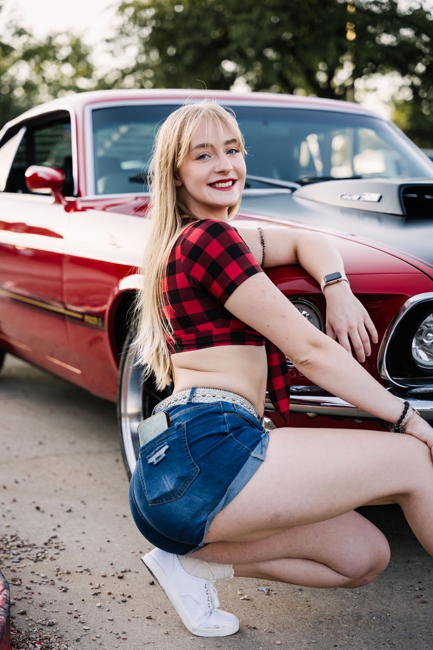 Fashion model poses next to a classic red car wearing buffalo plaid crop top and denim shorts.