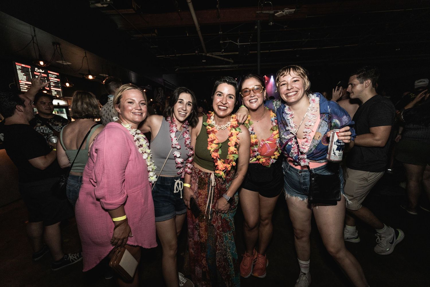 Friends in colorful outfits pose together at indoor music event.