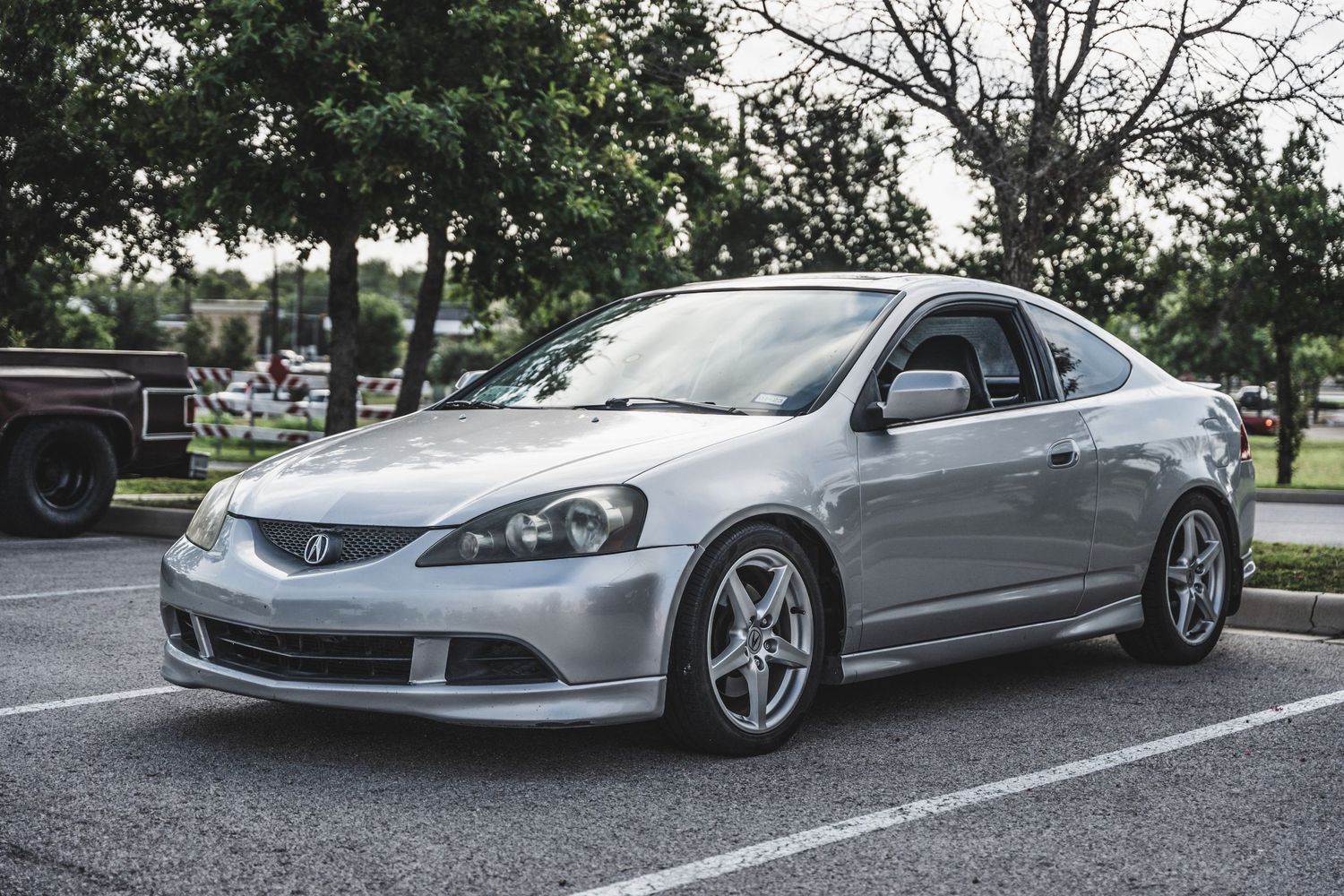Silver Acura RSX Type-S with aftermarket wheels parked in a lot.