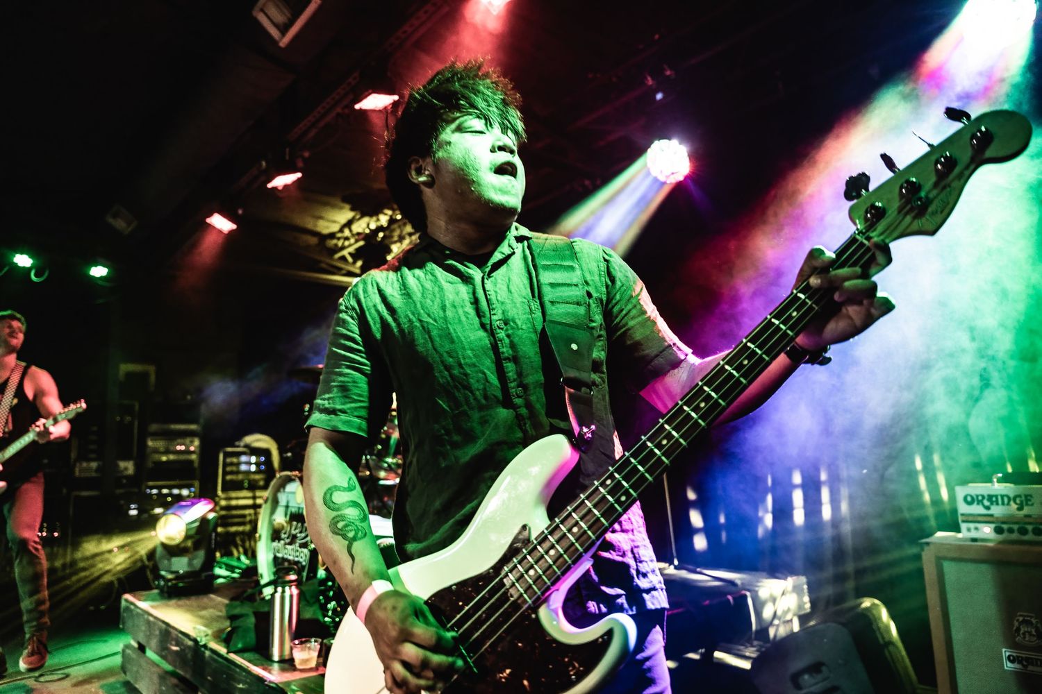Bass player performs energetically under dramatic green stage lighting during a rock show.