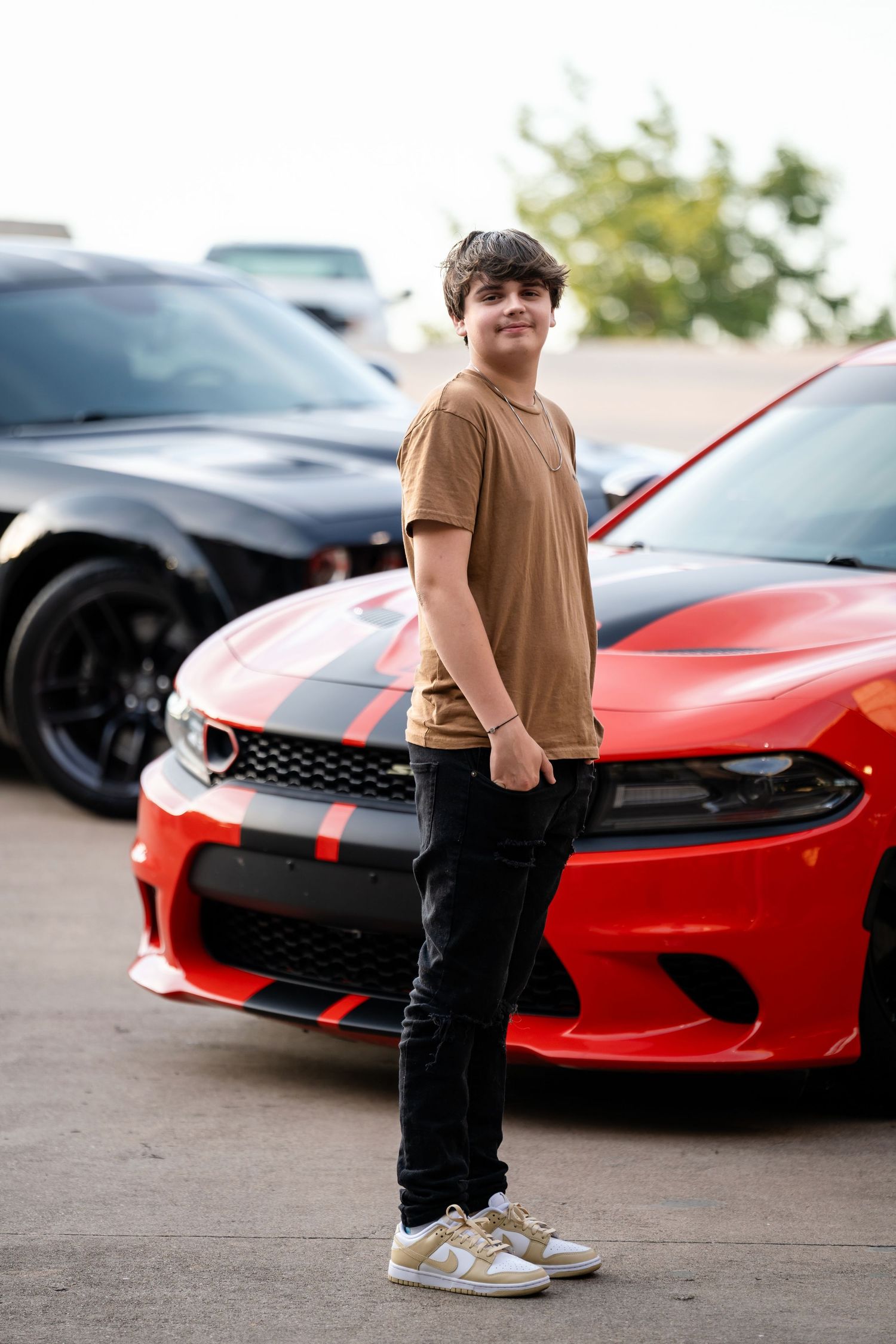 A casual portrait in front of a red and black Dodge Charger and black muscle car.